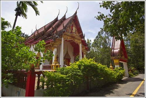 The golden and red building of the Wat Kathu Phuket against the green trees