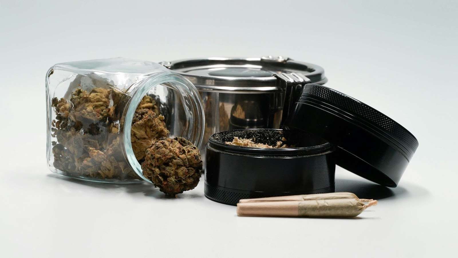 A glass jar with cannabis buds, a black grinder, and a pre-rolled joint.
