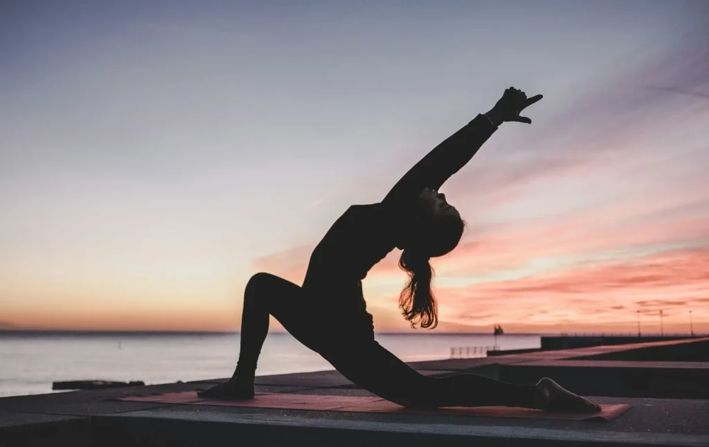 A woman doing a yoga pose on her mat while enjoying the sunset over the sea