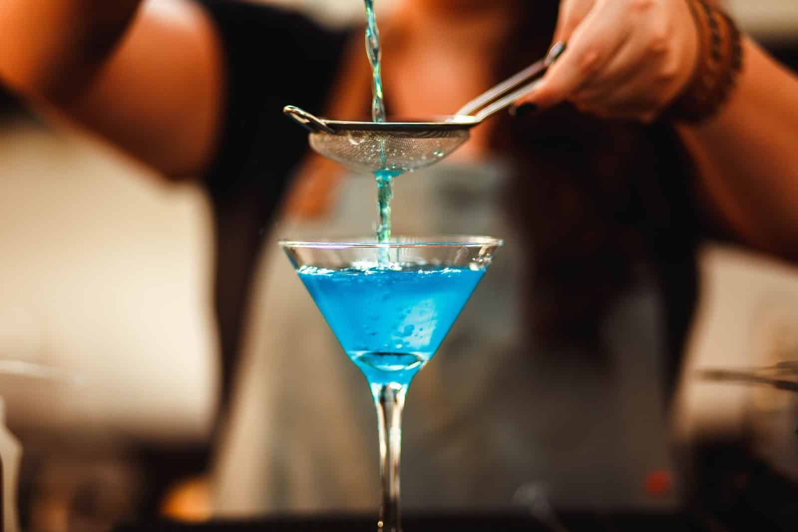 A glass of blue cocktail drink crafted by a female barista.