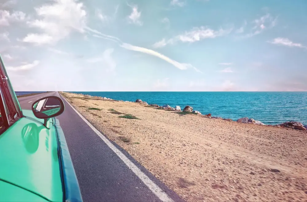 A green car driving along the beach coast